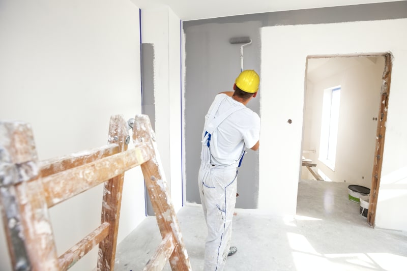 Home interior painter rolling paint on wall in bedroom.